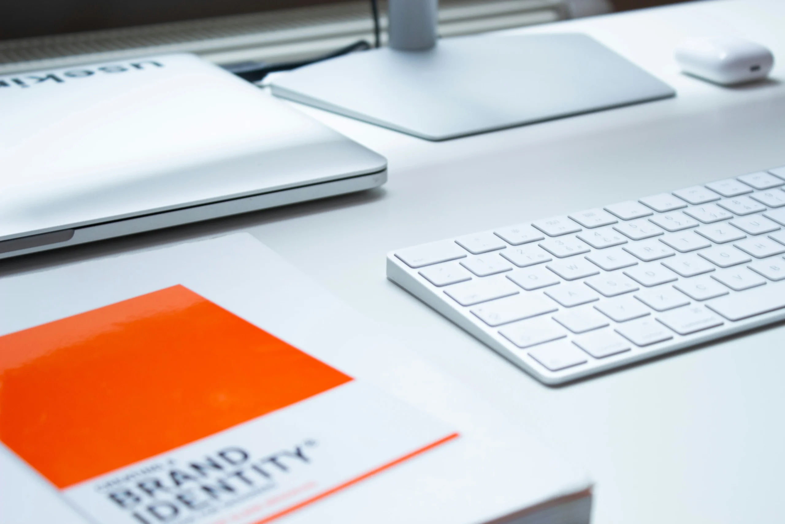 A picture of a white keyboard on a desk showing an orange book about best practices for the brand.
