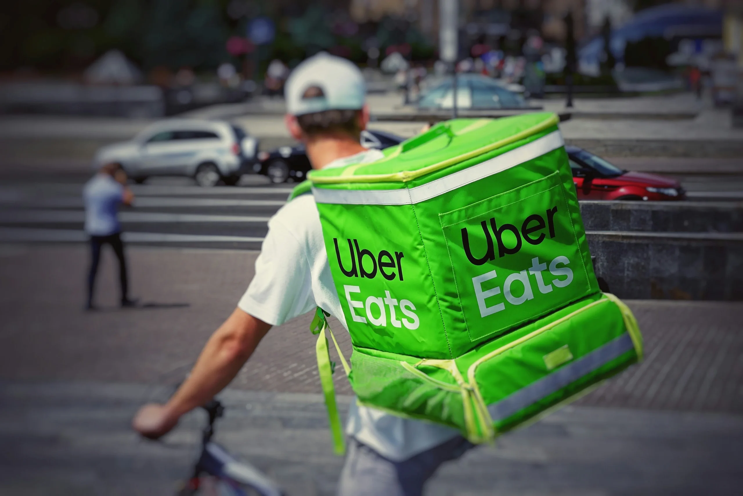 An uber eats delivery man on a bike with a green bag. 