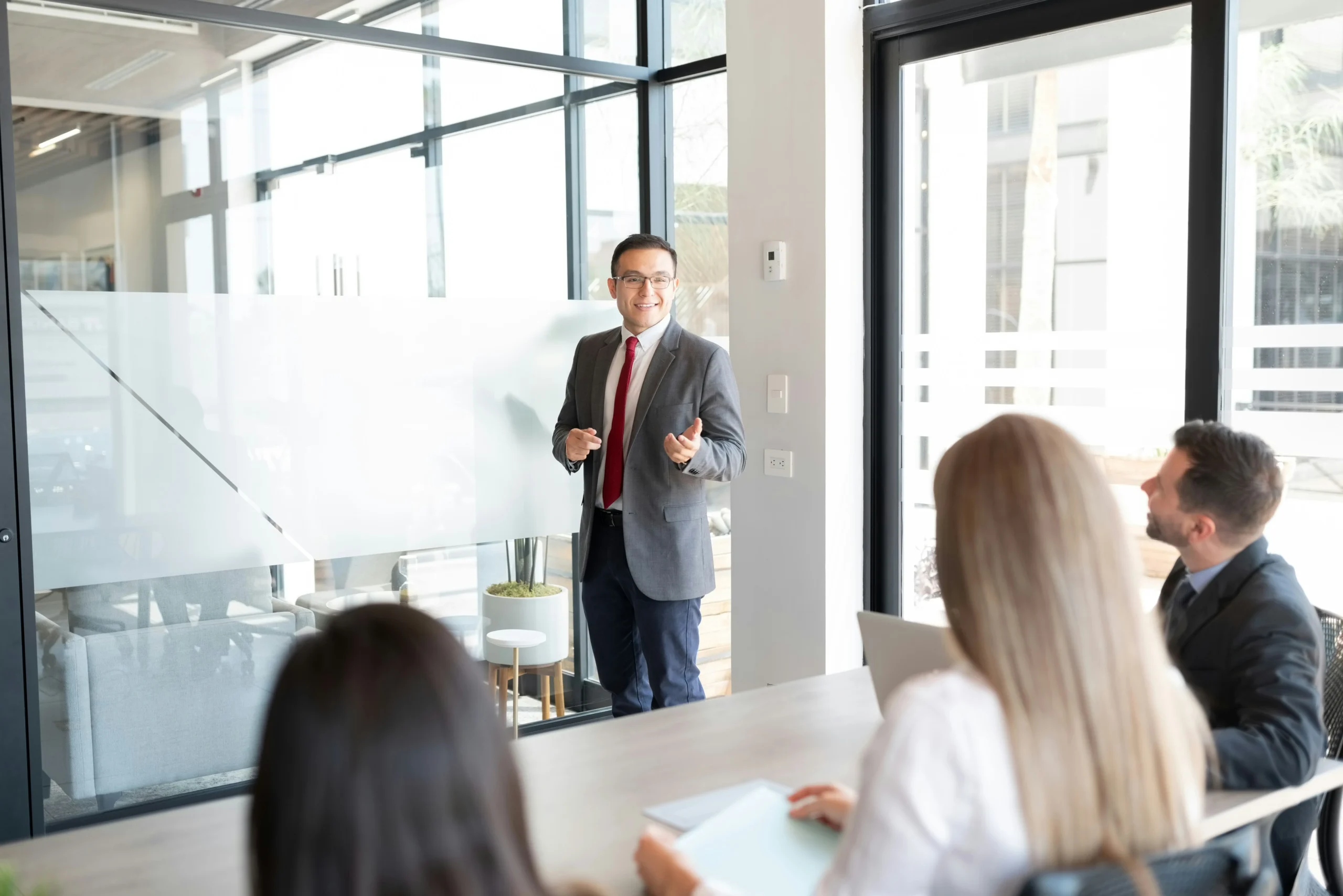 A man in a business suit standing in front of two staff while talking by a white board. This demonstrates what leaders of inspirational brands look like.